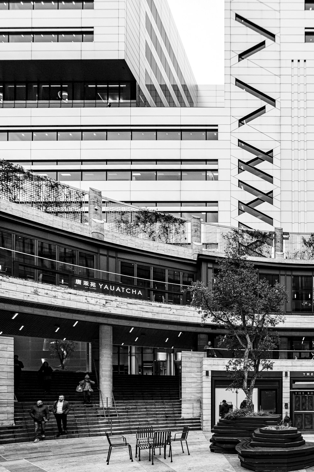 grayscale photo of people walking on sidewalk near building