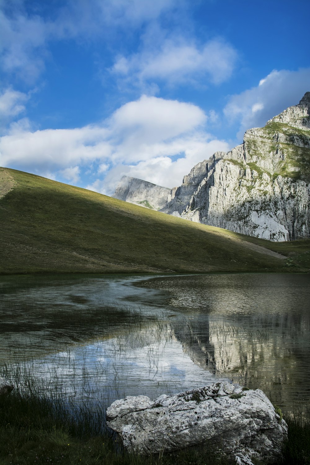 green and white mountain beside body of water under blue sky during daytime