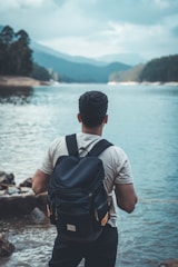 man in gray shirt and black backpack standing on rocky shore during daytime