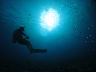 Close-up of a diver’s calm face with bubbles rising, illuminated by turquoise ocean light.