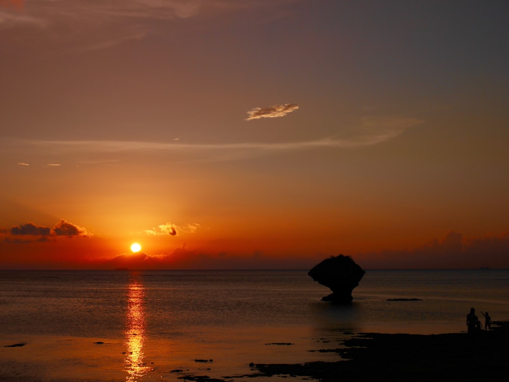 silhouette of rock on sea during sunset