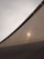 A close-up view of a fabric canopy, with sunlight creating a bright spot on the textured surface. The canopy is stretched taut, with visible seams or supports. The sky in the background is overcast, adding a muted tone to the overall scene.