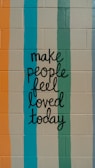 A motivational message is painted on a brick wall, featuring hand-lettered text that reads 'make people feel loved today.' The background consists of vertical stripes in various colors.