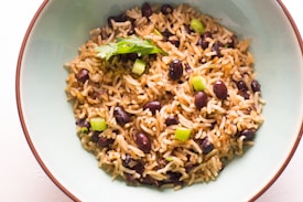 A bowl of seasoned rice mixed with black beans and garnished with chopped scallions and a sprig of parsley. The dish is served in a light blue bowl placed on a white surface.