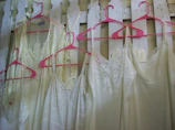 A soft pink blouse with delicate white lace details displayed on a wooden hanger.