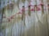 Several lacey white dresses or nightgowns are hanging on bright pink hangers against a white wooden fence. Each garment has a tag attached to it.