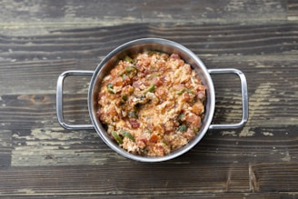A stainless steel bowl filled with a mixture of scrambled eggs, tomatoes, and green peppers, placed on a rustic wooden surface.