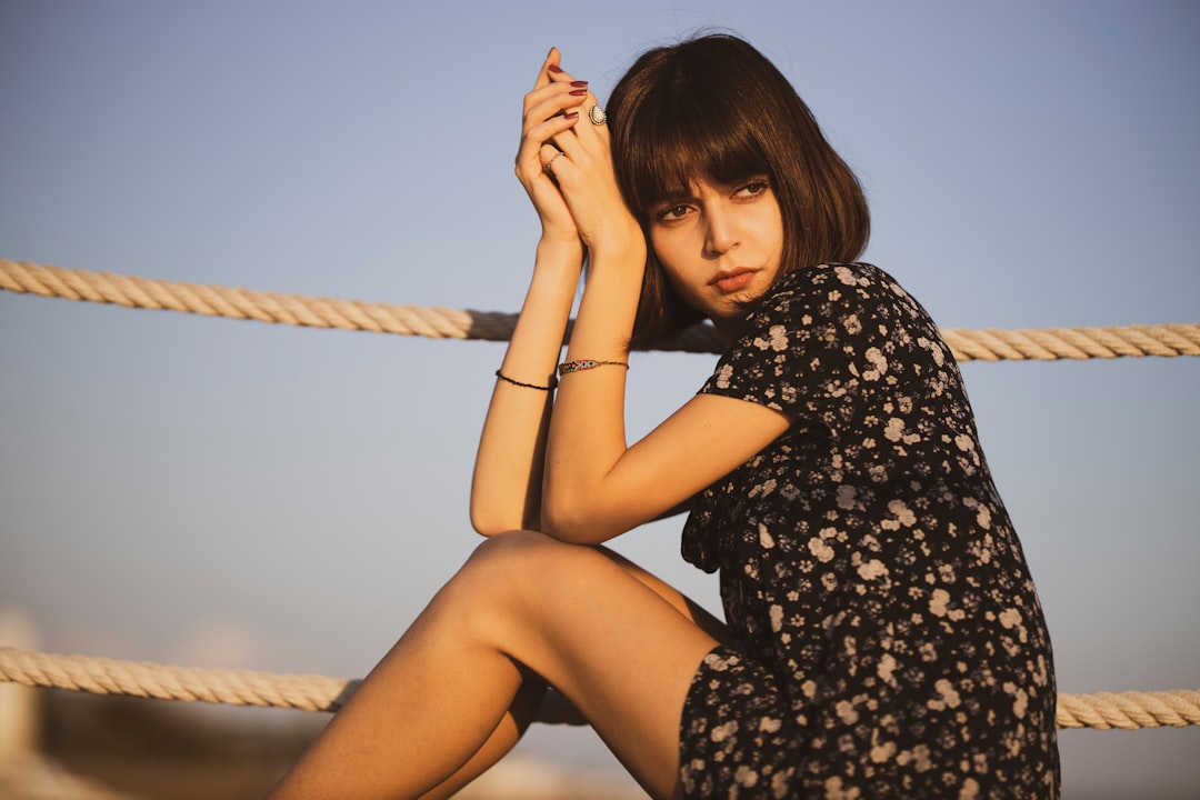 woman in black and white floral dress sitting on brown wooden swing during daytime