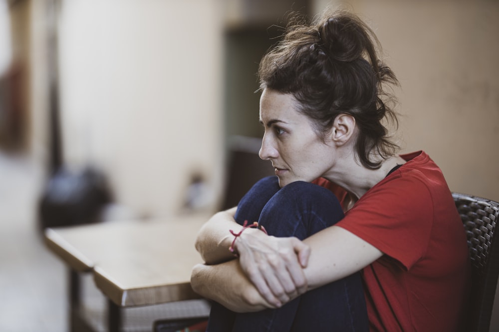 woman in red shirt sitting on brown wooden chair