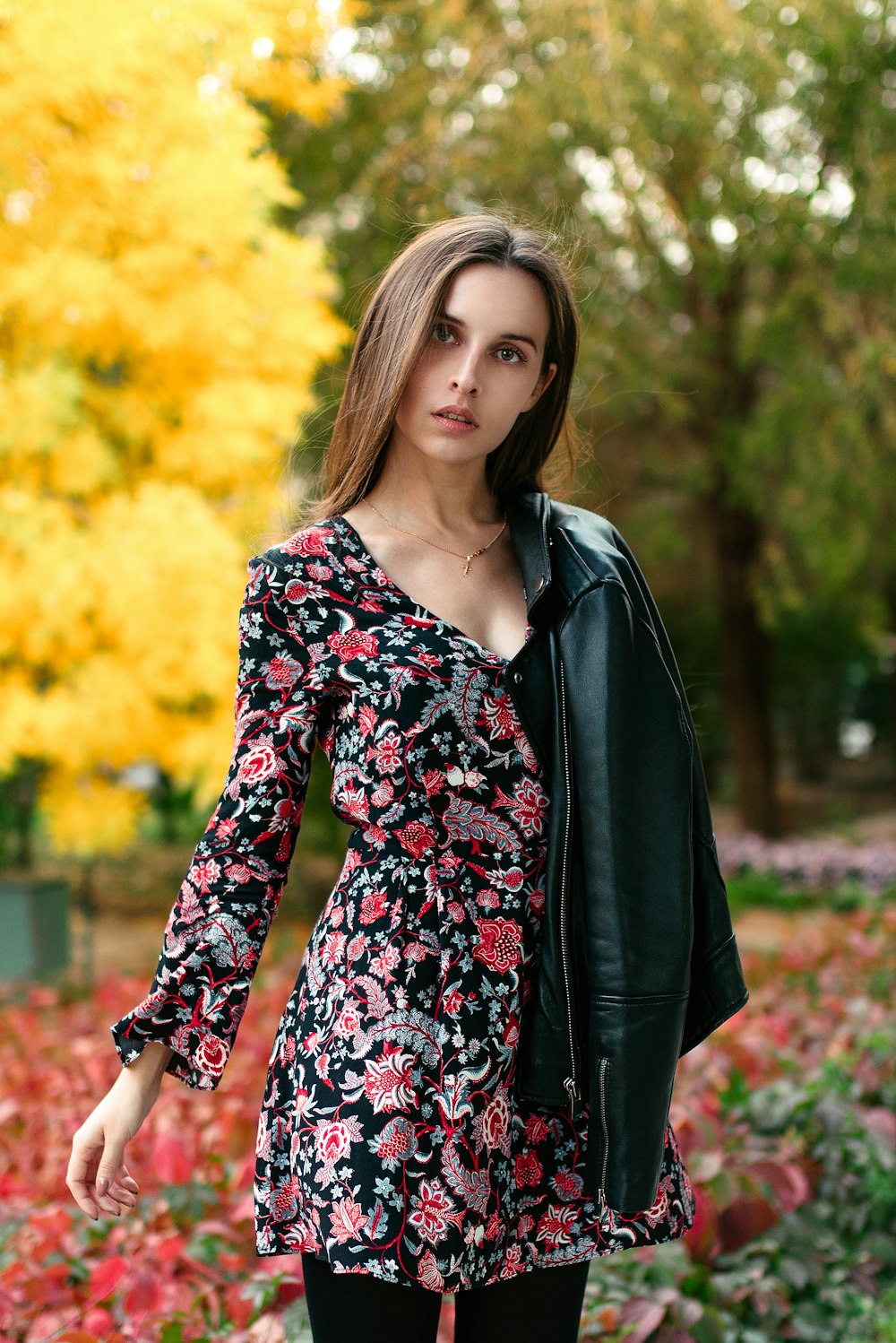 woman in black leather jacket standing near yellow leaf trees during daytime