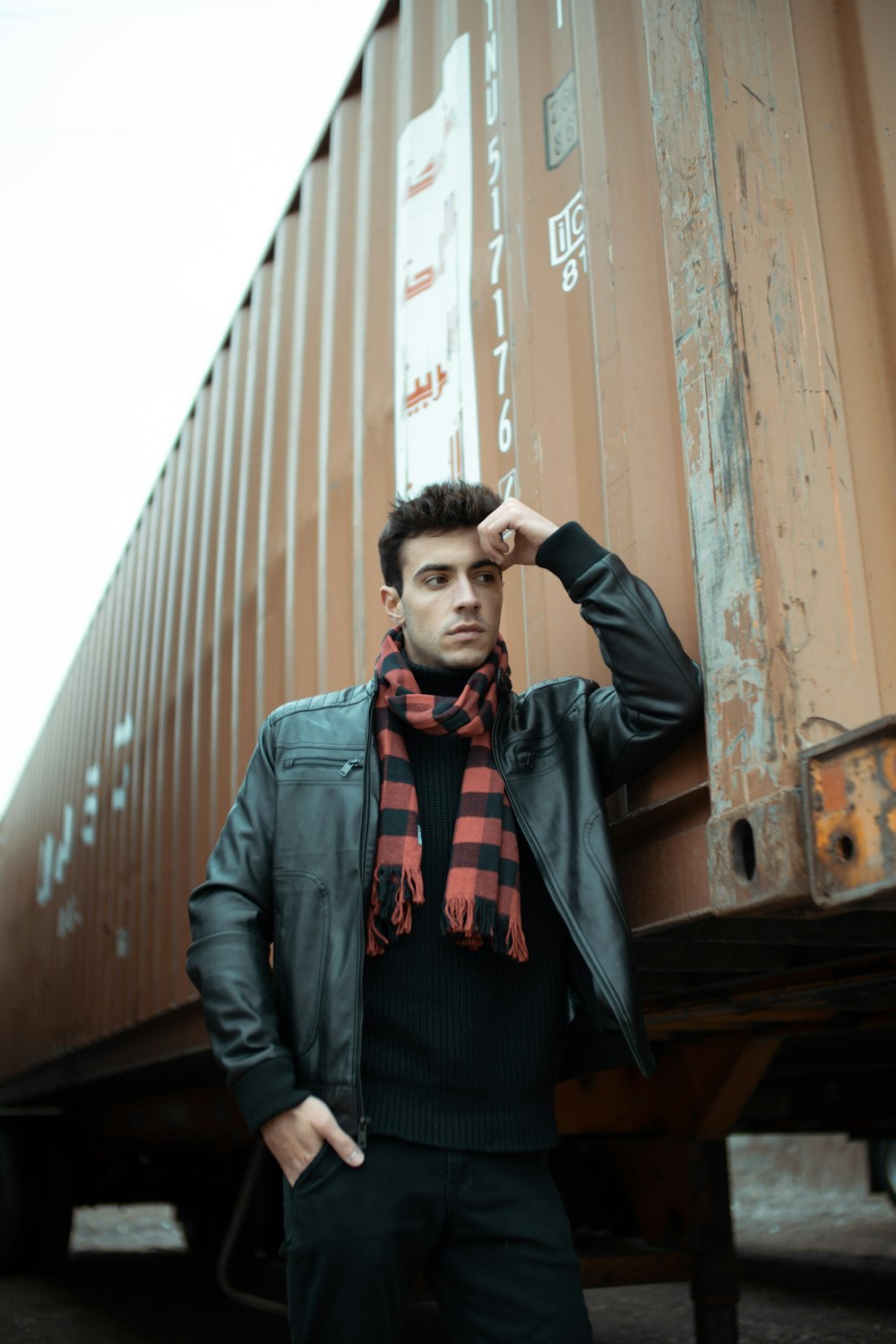 man in black leather jacket standing beside brown concrete wall during daytime