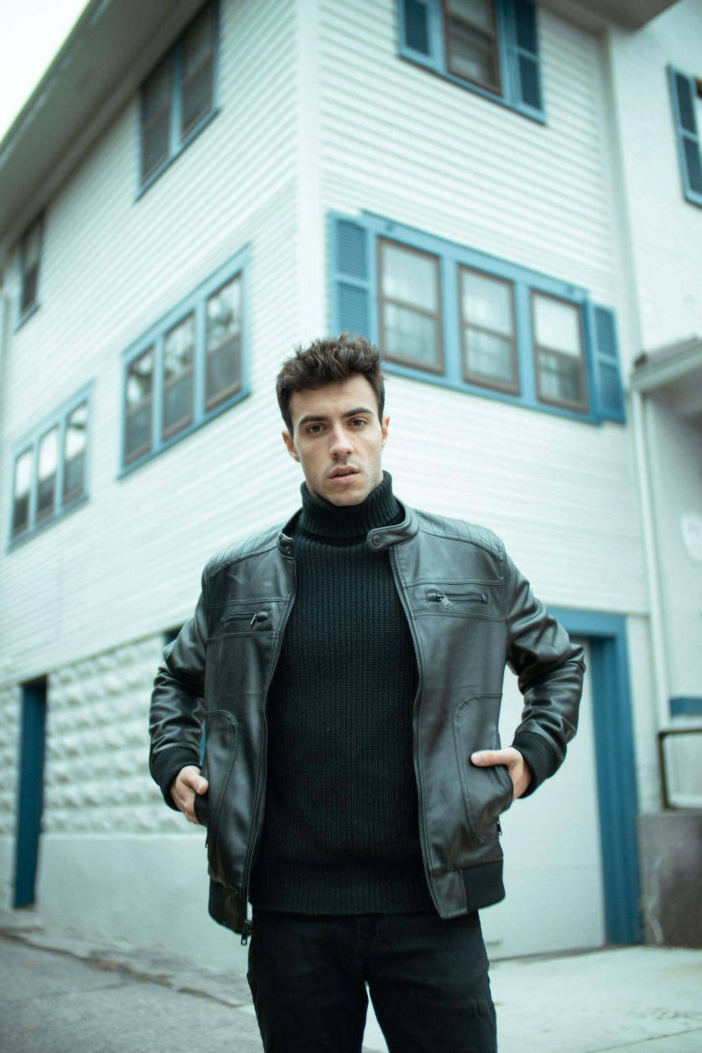 man in black leather jacket standing near white building during daytime