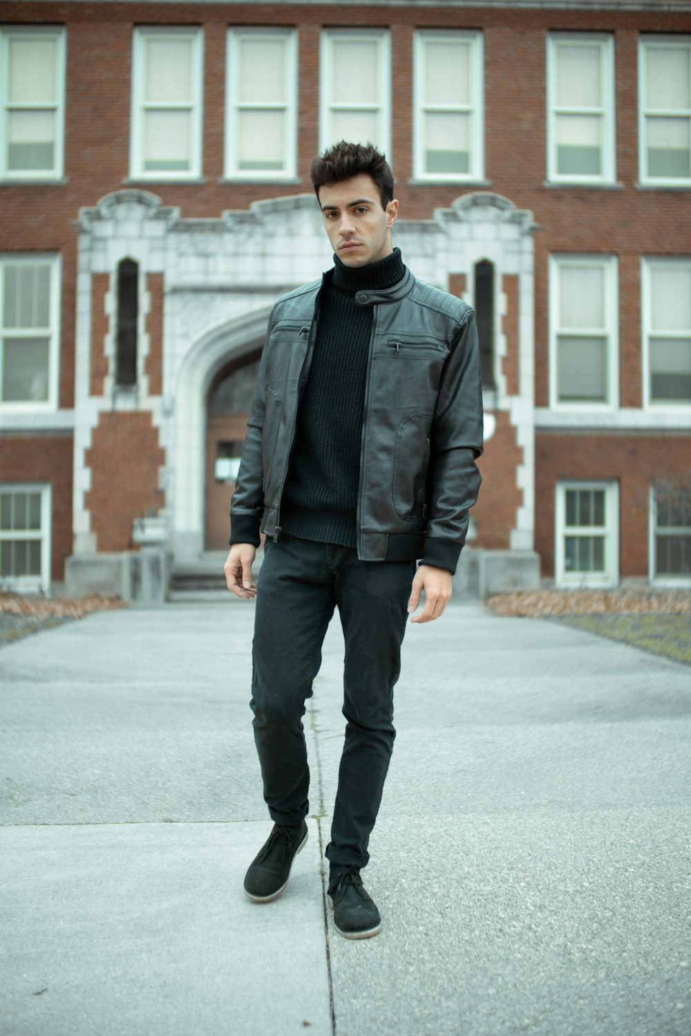 man in black leather jacket standing on sidewalk during daytime