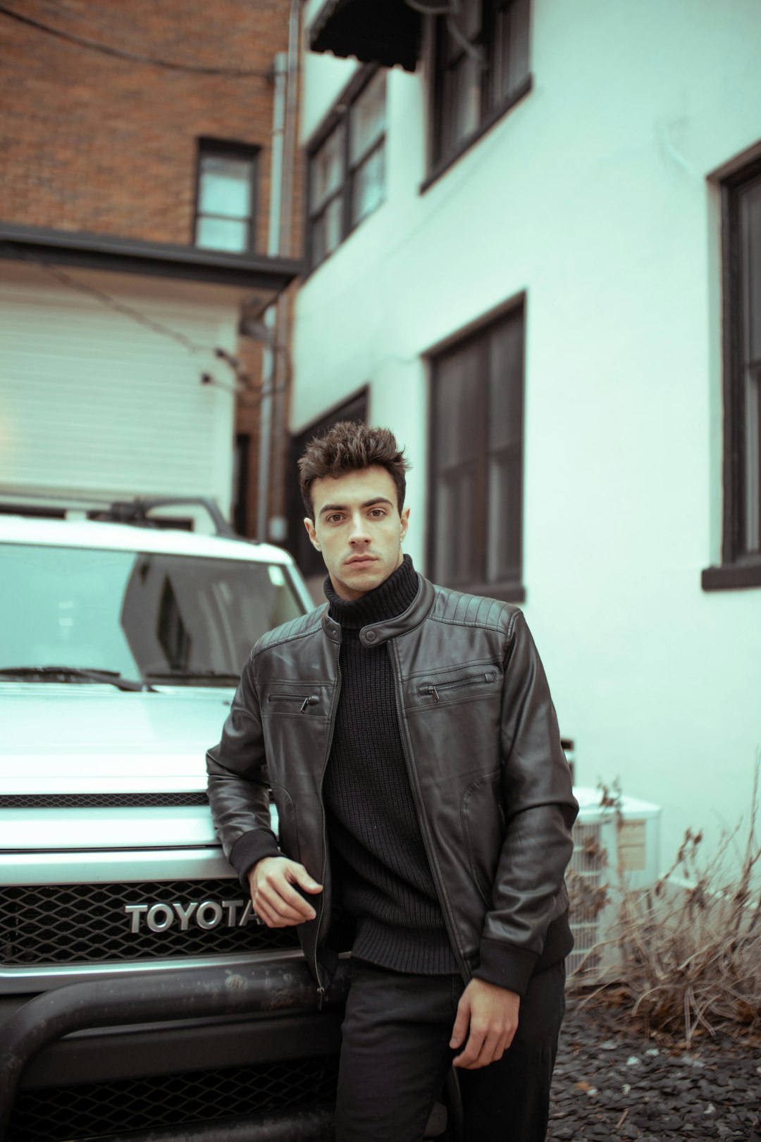 man in black leather jacket standing beside white car during daytime