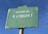 A green street sign with white text displaying 'Avenida de D. Carlos I'. The sign shows signs of wear with chipped paint and rust. The background is a clear blue sky.