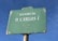 A green street sign with white text displaying 'Avenida de D. Carlos I'. The sign shows signs of wear with chipped paint and rust. The background is a clear blue sky.