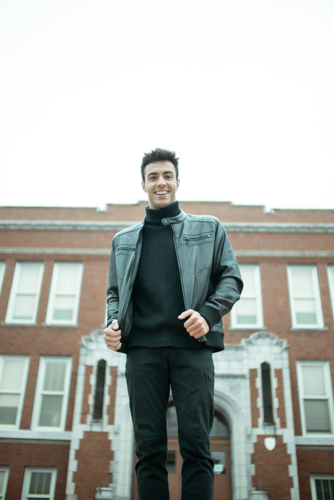 man in black leather jacket standing near brown concrete building during daytime