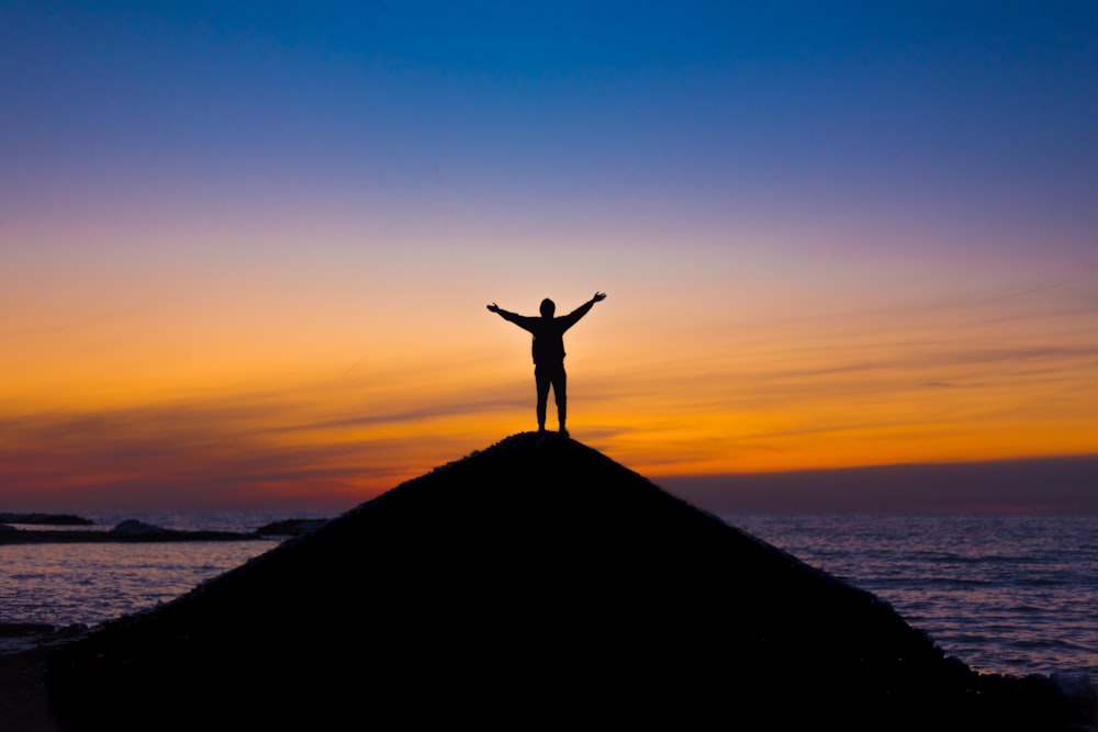 silhouette of person standing on rock during sunset