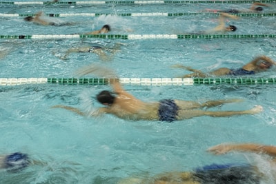Several swimmers are actively participating in a swim race, showcased by their dynamic movements in separate lanes of a swimming pool. Their synchronized strokes create splashes and ripples, emphasizing the competitive nature of the event.