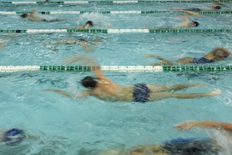 Several swimmers are actively participating in a swim race, showcased by their dynamic movements in separate lanes of a swimming pool. Their synchronized strokes create splashes and ripples, emphasizing the competitive nature of the event.