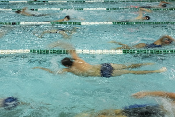 Several swimmers are actively participating in a swim race, showcased by their dynamic movements in separate lanes of a swimming pool. Their synchronized strokes create splashes and ripples, emphasizing the competitive nature of the event.