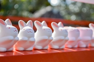 white and pink ceramic cat figurines on red wooden shelf