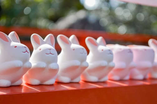 white and pink ceramic cat figurines on red wooden shelf