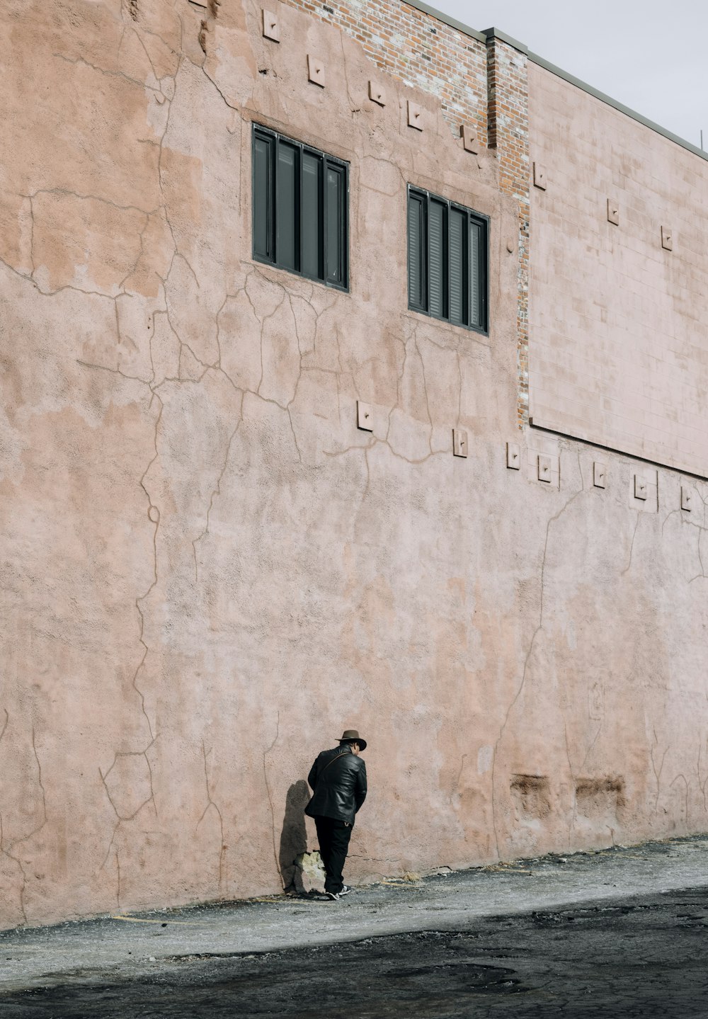 man in black jacket and black pants standing beside brown concrete wall during daytime