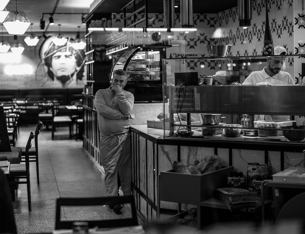 grayscale photo of woman in long sleeve shirt standing near counter