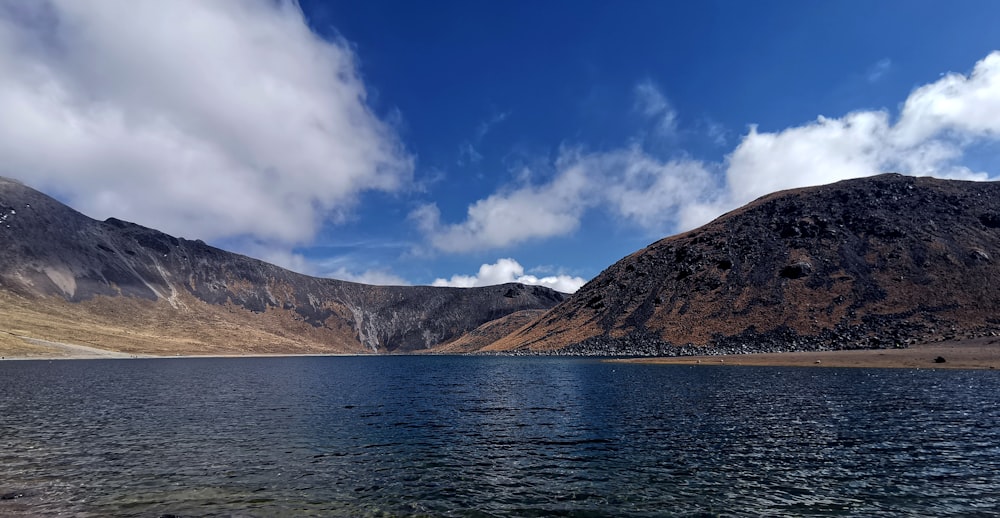 brown mountain beside body of water under blue sky during daytime