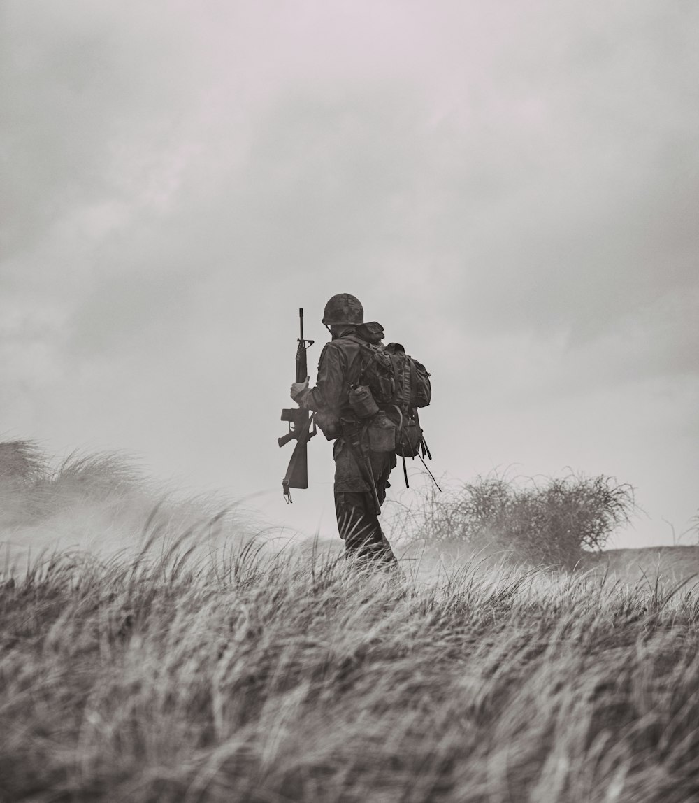 grayscale photo of man in black jacket and pants holding rifle