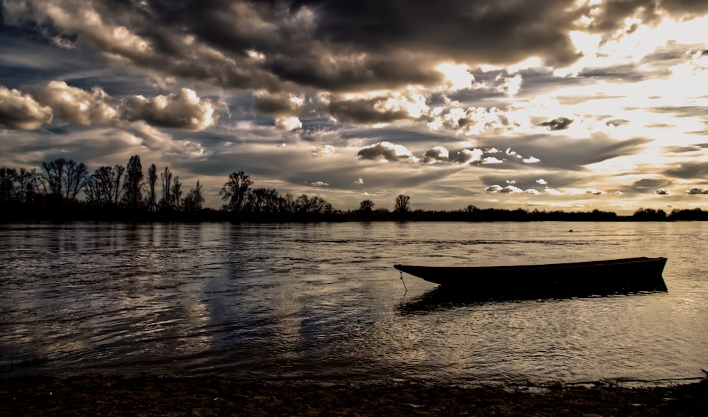 silhouette of trees and boat on water during sunset