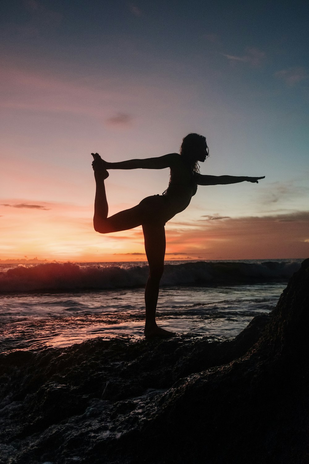 silhouette of woman standing on rock during sunset