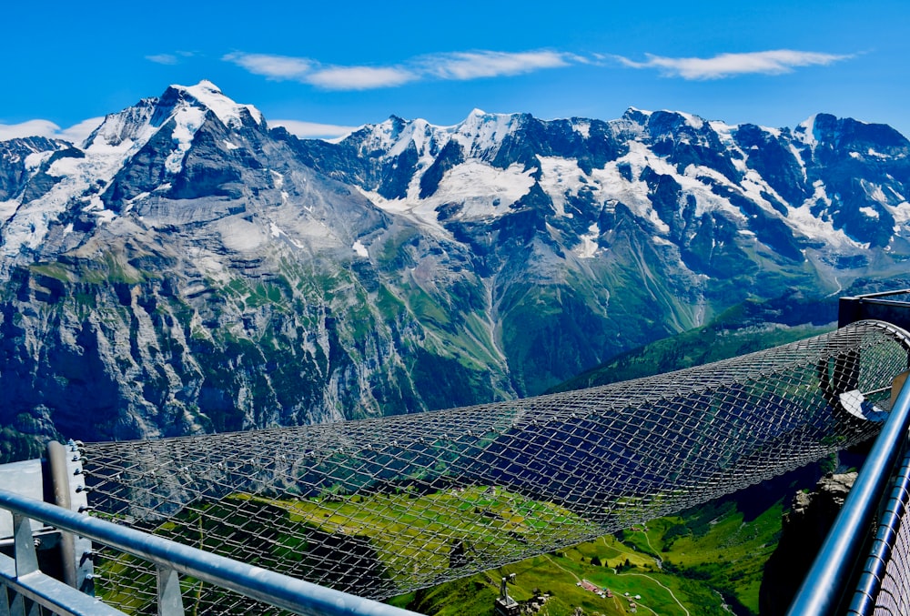 gray metal fence near green grass field and snow covered mountains during daytime