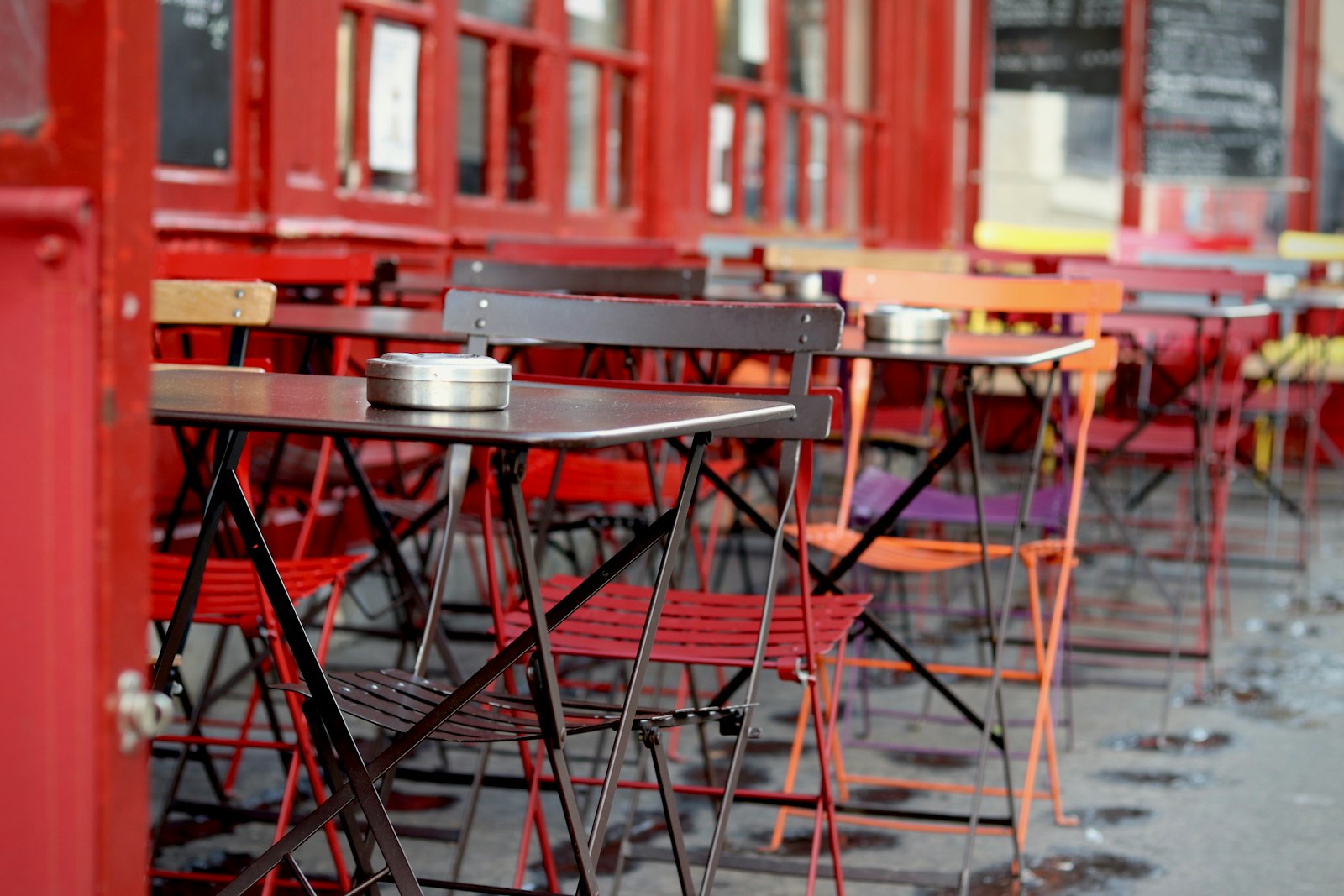 Colorful folding bistro chairs and small tables on an empty Paris café terrace after rain