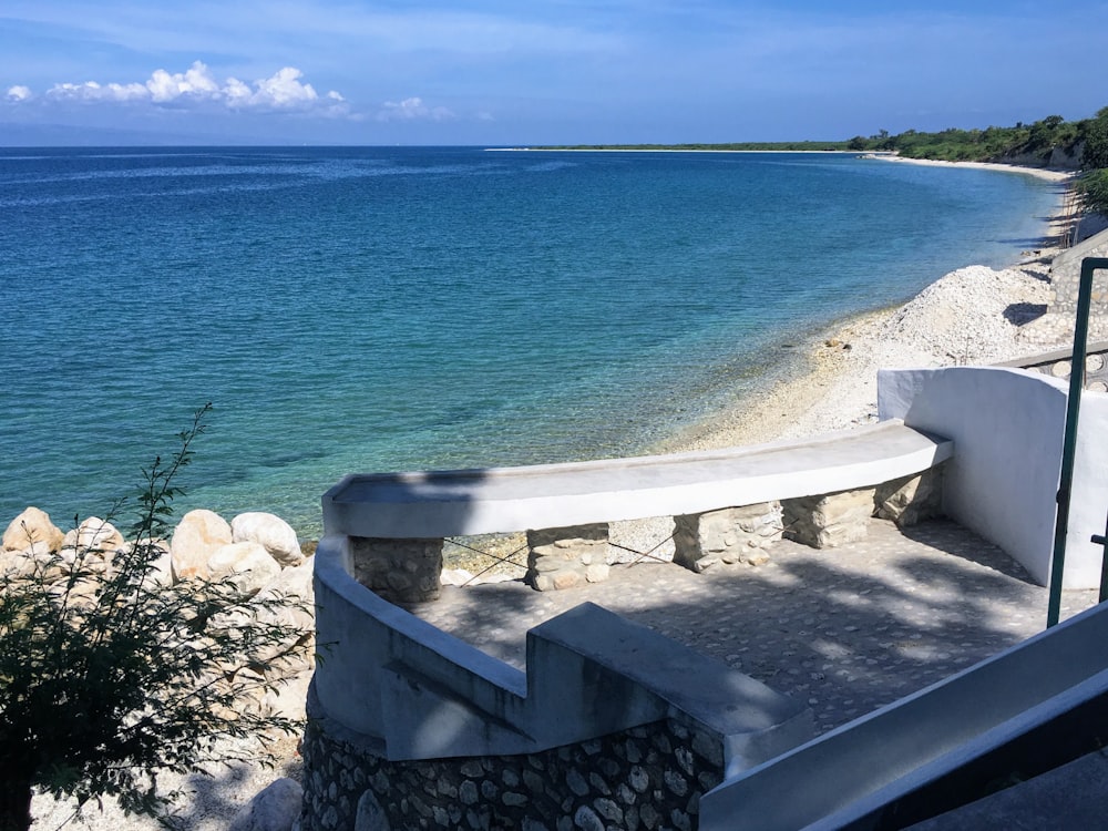 white concrete bench near blue sea under blue sky during daytime