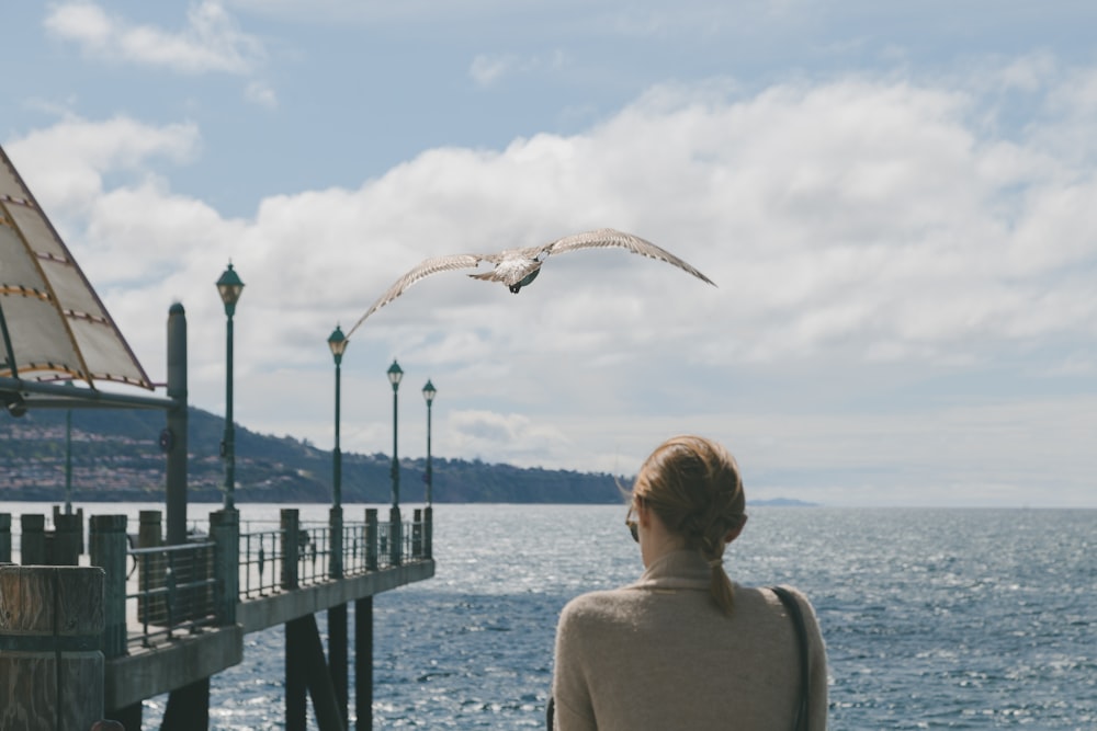 mujer en camiseta blanca sin mangas mirando a los pájaros que vuelan sobre el mar durante el día