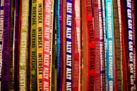 Colorful ribbons featuring words related to gender identity and sexual orientation hang vertically. Each ribbon displays labels like lesbian, bisexual, intersex, transgender, and ally, among others. The ribbons are in a vibrant array of shades, creating a rainbow effect.
