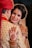 A bride adorned in traditional Indian attire, featuring detailed jewelry and henna designs while embracing her partner. The bride is smiling, with decorative elements including a bindi, earrings, and an intricate hairstyle.