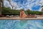 woman in pink dress sitting on brown wooden bench near swimming pool during daytime