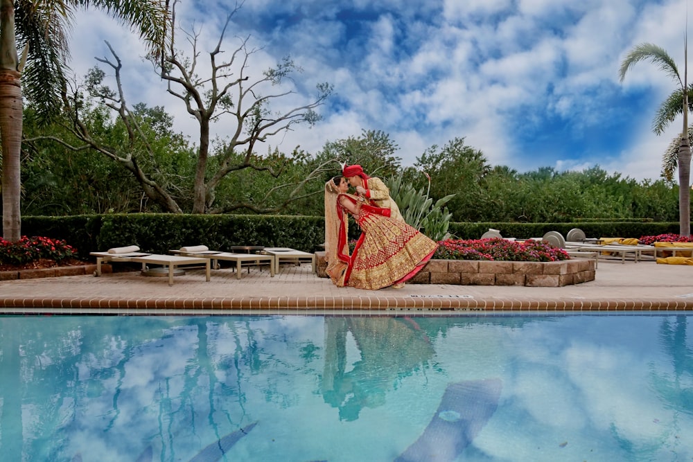 woman in pink dress sitting on brown wooden bench near swimming pool during daytime