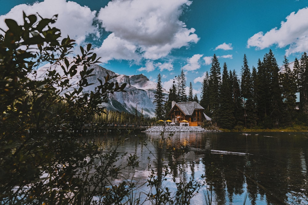 Casa di legno marrone vicino agli alberi verdi e alla montagna sotto le nuvole bianche ed il cielo blu durante il giorno