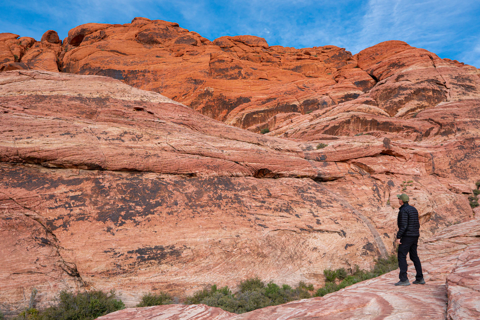 Hiker standing beneath sweeping red sandstone cliffs