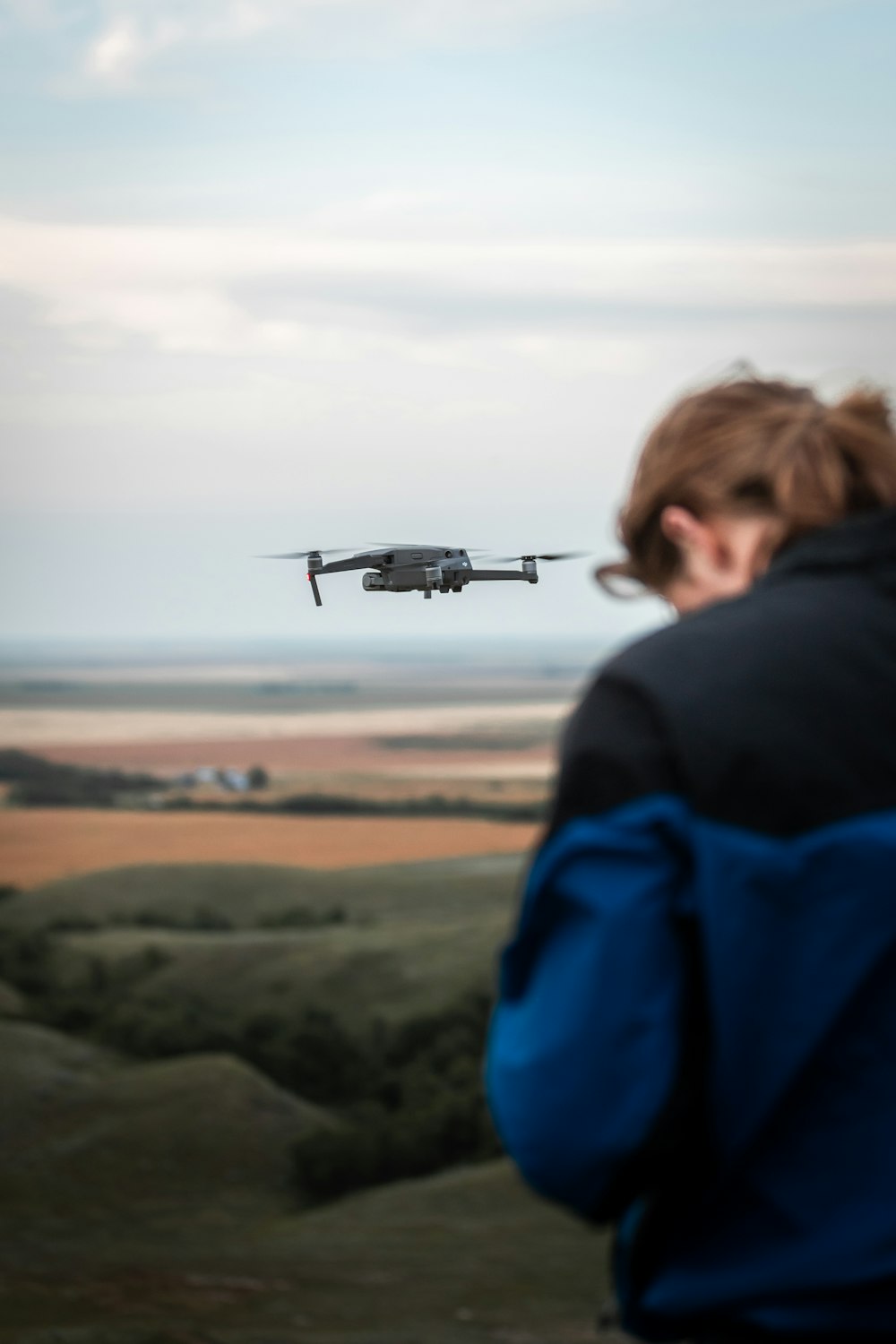 man in blue jacket looking at gray drone