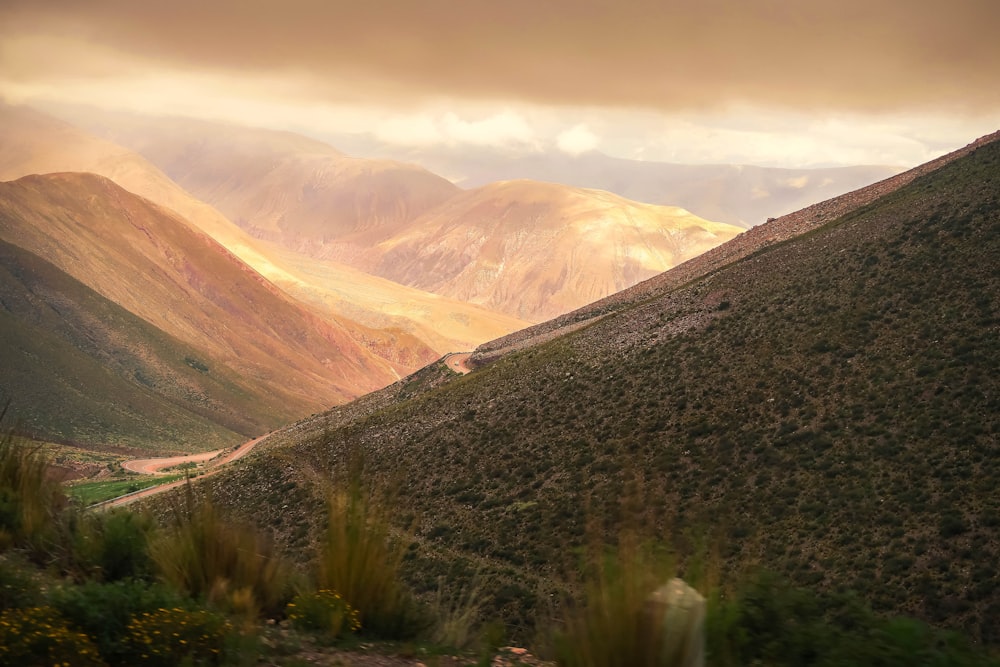 campo di erba verde vicino a montagna marrone sotto nuvole bianche durante il giorno