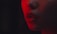 A close-up shot of a person's lower face, focusing on their nose and slightly parted lips. The lighting is dramatic, with a strong red hue casting shadows and enhancing features like the nose ring.