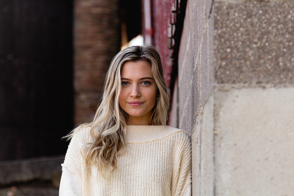 woman in white turtleneck sweater standing beside gray concrete wall