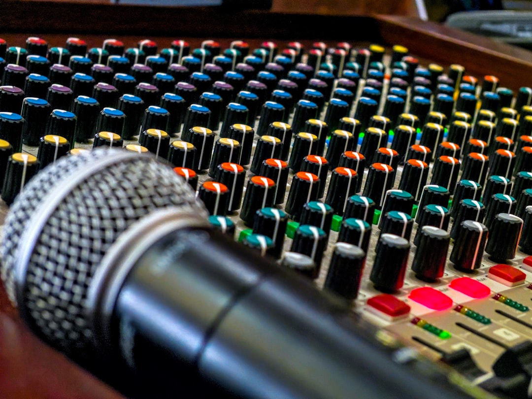 A microphone rests on a live sound mixing board containing colorful knobs. 