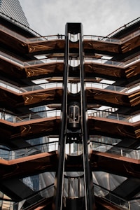 A futuristic architectural structure with multiple levels and a central vertical element resembling an elevator shaft. The design features a mix of metallic and glass materials with geometric patterns.