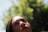 A close-up of a person looking upwards with a thoughtful expression. The background consists of lush greenery out of focus, suggestive of a natural setting.